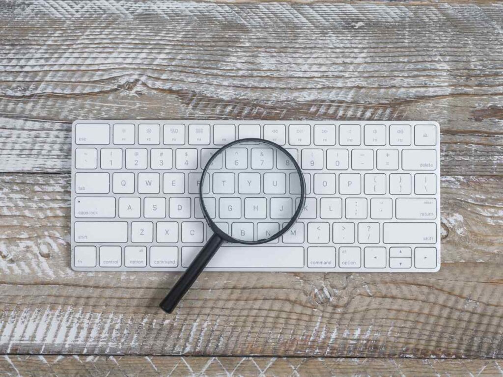 lupa sobre teclado branco a simbolizar a pesquisa de plágio com IA