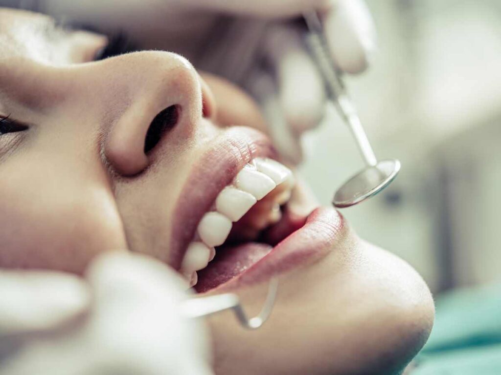 Close-up da boca de um paciente sendo examinado por um dentista, simbolizando o trabalho clínico em odontologia.