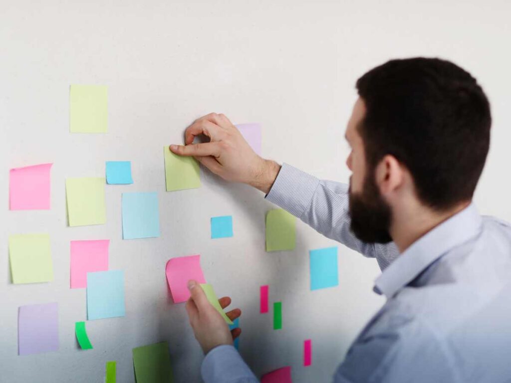 Homem a organizar post-its coloridos em uma parede, simbolizando planejamento e organização para a elaboração de uma tese.