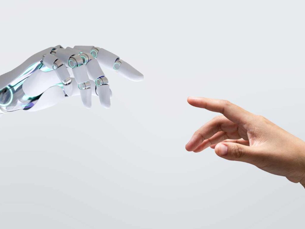 Mão humana prestes a tocar a mão de um robô, simbolizando a interação entre humanos e inteligência artificial em projetos acadêmicos.