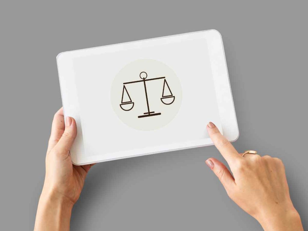 Mãos a segurar um tablet com ícone de balança jurídica, ilustrando dúvidas sobre a legalidade de pedir um projeto de mestrado.